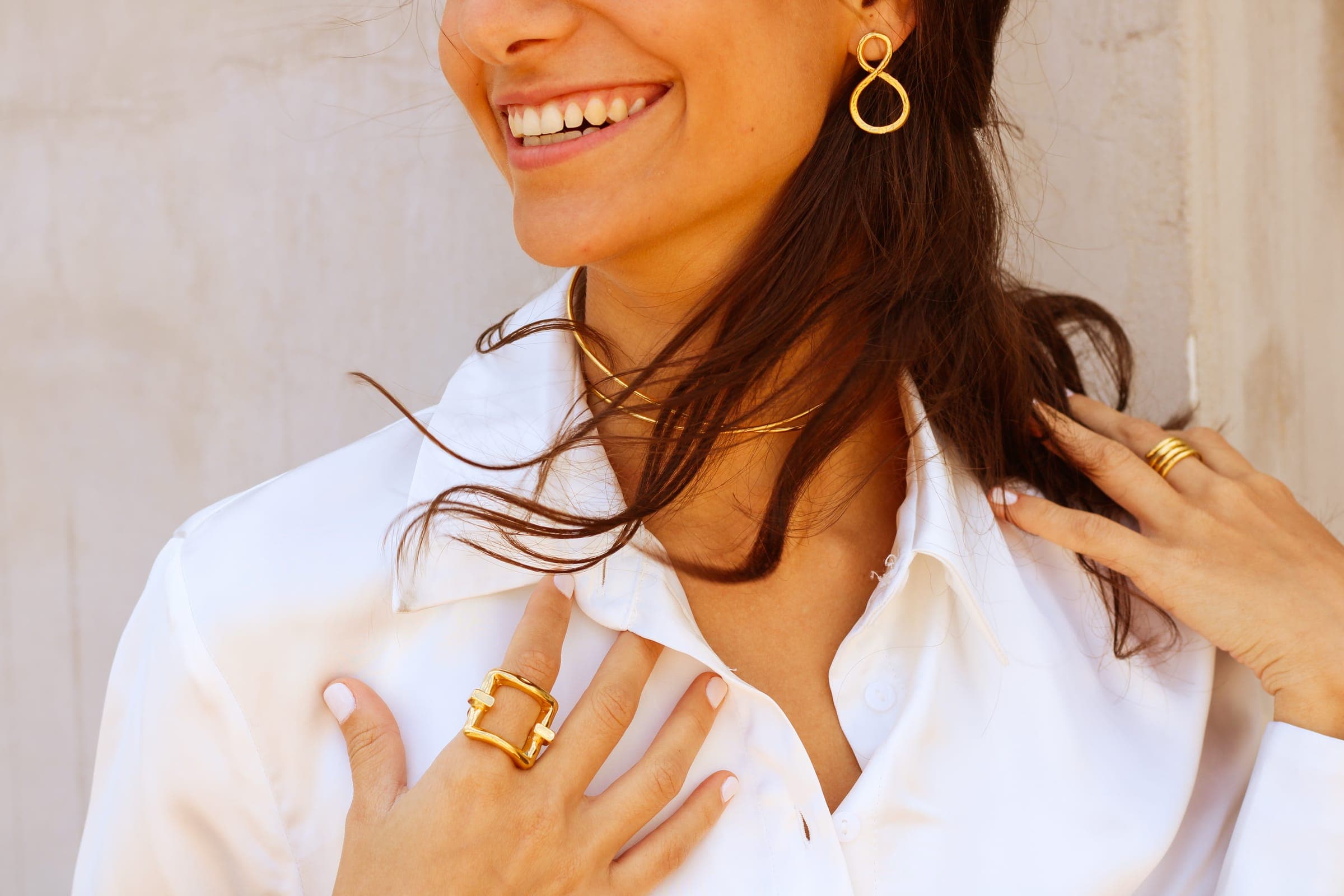 Mujer con blusa blanca luciendo aretes, gargantilla y anillo dorados hechos a mano